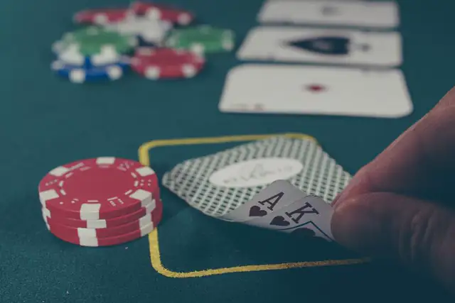 Player lifting the corner of two cards beside a stack of chips on green felt